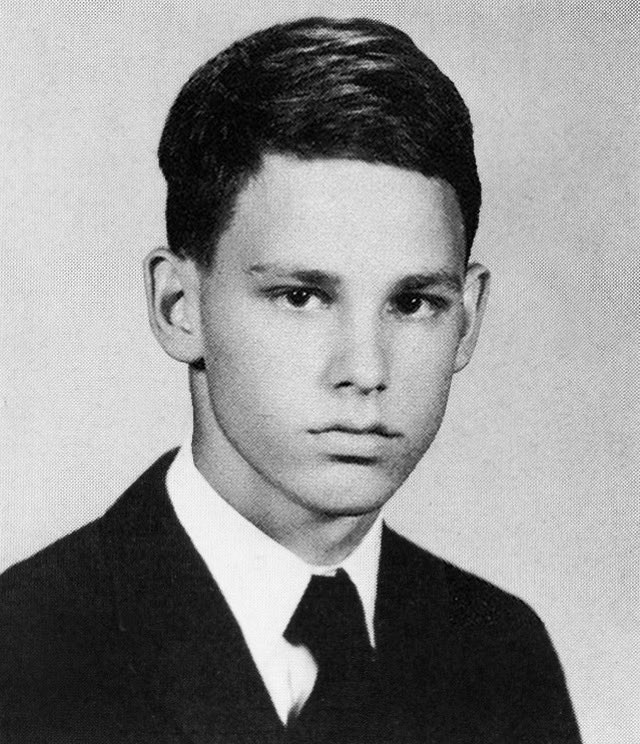 Black-and-white yearbook portrait of seventeen-year-old James Douglas Morrison from the 1961 George Washington High School yearbook in Alexandria, Virginia. Three-quarter view, side-parted dark hair, dark coat over white shirt and dark tie, photographed against a plain light backdrop.
